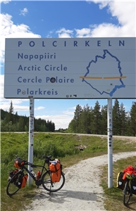 Fahrrad mit Packtaschen parkt an einem Straßenschild mit der Aufschrift "Polarkreis" in mehreren Sprachen