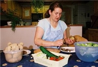 Frau sitzend am Tisch, beim Gemüse schneiden